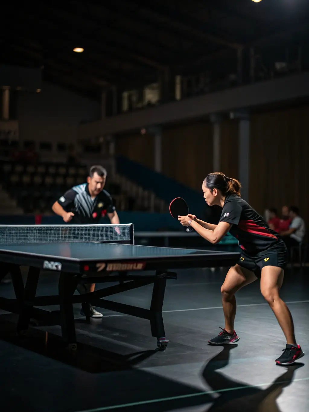 An action shot of adult players engaged in a friendly yet competitive table tennis match, with spectators and a referee visible, emphasizing camaraderie and skill.